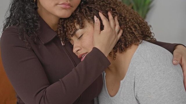 Woman cradles head and strokes curly hair while hugging on a bed in a bedroom, hand on shoulder and palm at neck; comfort intimacy.