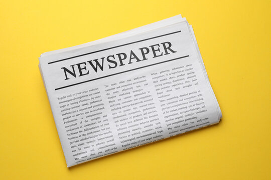 Folded newspaper on orange background, top view