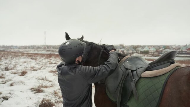 Person securing horse gear carefully. Individual adjusting harness while caring for snowy equine surroundings. Tender horse handler making sure equipment is secure in cold winter landscape