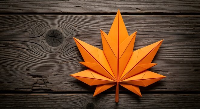 Vibrant orange origami maple leaf resting on weathered wooden surface