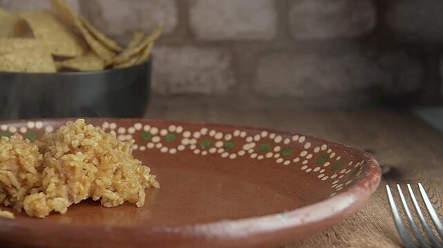 Mexican rice, served on a handmade clay plate, on a rustic wooden table with a brick wall in the background, serving mole poblano
