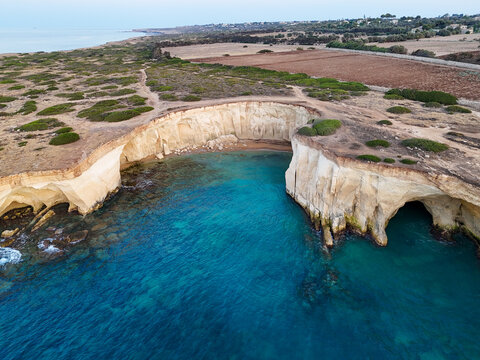 Aerial view of the white limestone cliffs and turquoise waters of Cala Bianca cove along the rugged coastline in Syracuse, Sicily, Italy.