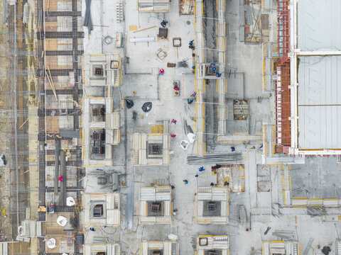 Aerial view of a busy construction site with workers in colorful safety vests moving among rebar structures and concrete foundations in Taiwan.