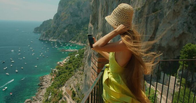 Woman in dress taking photo at Gardens of Augustus viewpoint overlooking Marina Piccola in Capri Italy