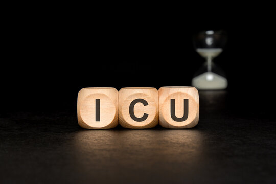 ICU - Intensive Care Unit - acronym on wooden blocks. Dark medical concept with hourglass.