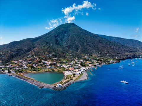 Aerial view of Salina island featuring the village of Lingua with its salt lake and lighthouse under a volcanic peak in Metropolitan City of Messina, Sicily, Italy.