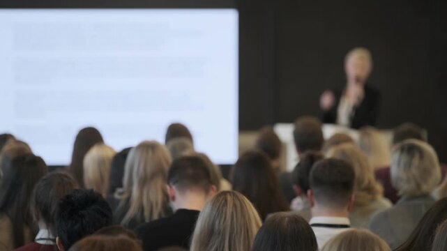 Conference audience listens to presenter during Tech Week seminar, blurred slide screen, professional networking atmosphere.