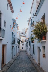 Spain, Altea city. Narrow cobblestone street lined with whitewashed buildings and colorful decorations in a charming Mediterranean village setting © JuLady_studio