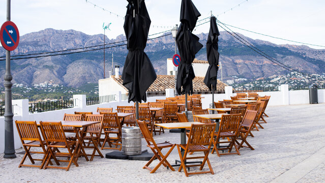 Spain, Altea city. Outdoor restaurant terrace with wooden tables and chairs, black umbrellas, and scenic mountain view in a Mediterranean setting