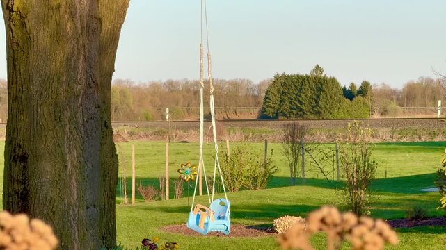 Child swing swaying slowly in the wind under a large tree in a green backyard