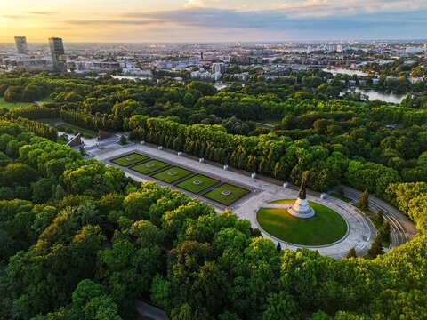 Aerial view of the Soviet War Memorial Treptow surrounded by lush green trees in Treptower Park with the city skyline under a golden sunset Berlin, Berlin, Germany.