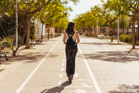 Anonymous lady with backpack riding scooter on pavement