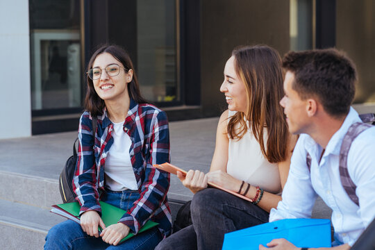 Positive college friends with notebooks chatting happily