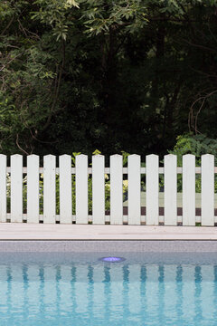 Swimming pool with white picket fence and greenery in the background