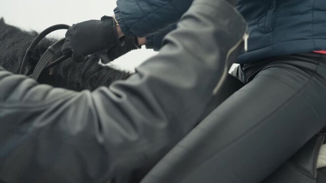 Closeup gloved hands on reins and saddle, rider adjusting grip and control during winter training, textured leather tack, quiet focused motion and disciplined connection between hand and horse.