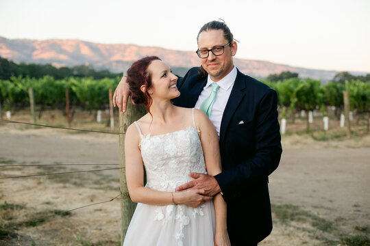 Smiling Bride and Groom Embrace in Vineyard at Sunset