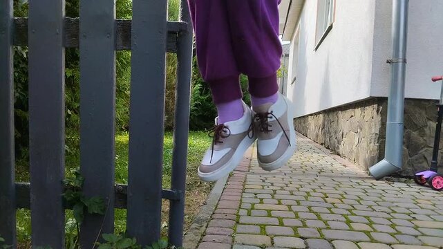 A child's feet in sneakers hanging in the air near a fence, Dynamic shot of a child's feet in purple sweatpants and stylish sneakers hanging in the air and feeding with their feet