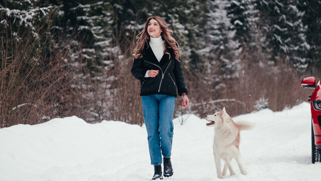 Woman with dog near red SUV in snowy forest