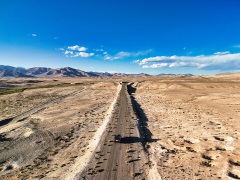 Aerial view of a vehicle driving on a remote road through the arid mountain landscape of Rabat Sasok-Kul, Viloyati Mukhtori Kuhis, Tajikistan.