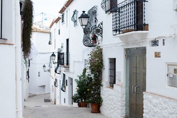 Fototapeta premium Spain, Altea city. Narrow street in a picturesque Spanish village with whitewashed buildings, decorative balconies, and vibrant flower pots lining the pathway