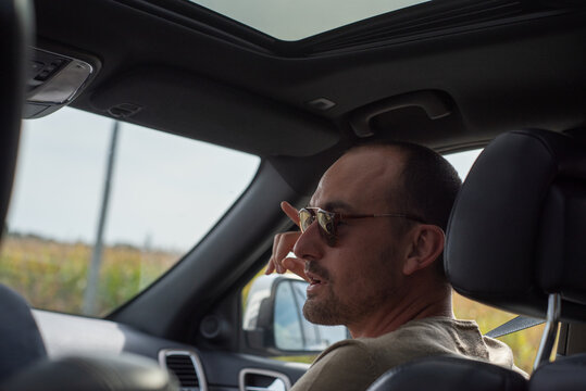 Man Sits in Car and Talks During a Road Trip on a Sunny Day