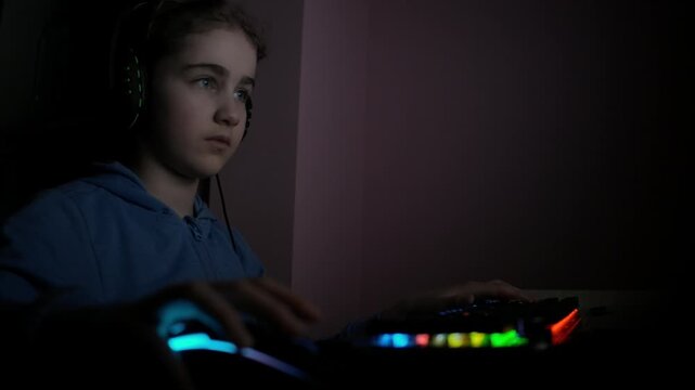 Girl Playing Video Game PC in Headset. Girl Plays Computer Video Game in Room, Cybersport Gaming, Children Gaming Addiction. Child Play Computer Game at Home. Online Video Game Technology.
