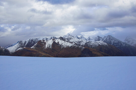 Snow plateau facing autumn ridges under cloudy sky, Swiss Alps