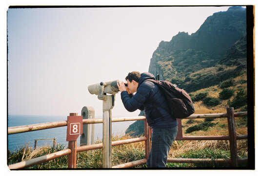 Man Uses Binoculars to View Ocean From Cliffside Lookout