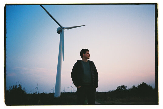 Man Standing Near Wind Turbine at Sunset in Rural Landscape