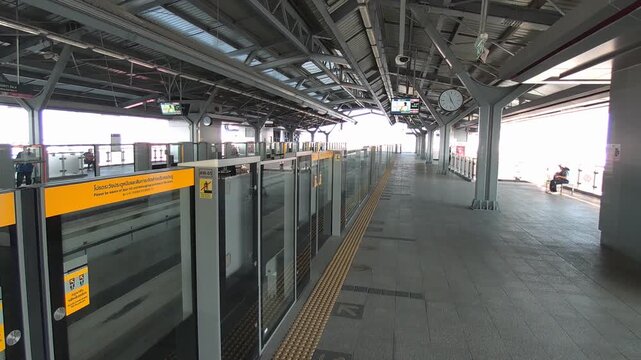 Cinematic footage capturing the calm atmosphere of an elevated skytrain station in Bangkok, Thailand during non-peak hours. The scene modern urban transportation infrastructure with minimal crowds