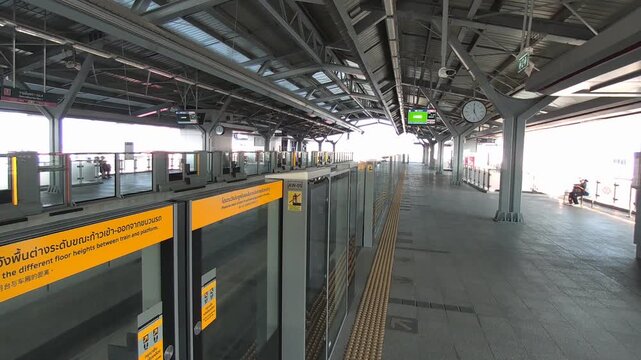 Cinematic footage capturing the calm atmosphere of an elevated skytrain station in Bangkok, Thailand during non-peak hours. The scene modern urban transportation infrastructure with minimal crowds