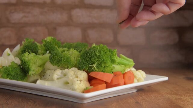 Steamed vegetables, carrots brocoli and cauliflower on a rectangular white plate to accompany meat, chicken or fish, on a rustic wooden table, with a brick wall in the background, ready to be seasoned