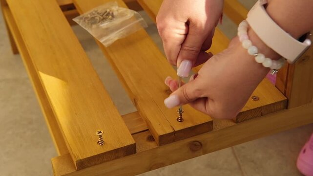 Close-up of woman hands using a hex key to tighten a screw while assembling wooden furniture, conveying DIY, craftsmanship, home improvement and careful manual work.