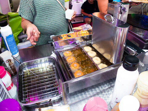 Street vendor frying mini donuts in hot oil at local market