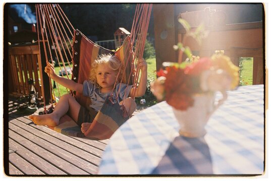 A blond boy is sitting on a hammock against the background of a table
