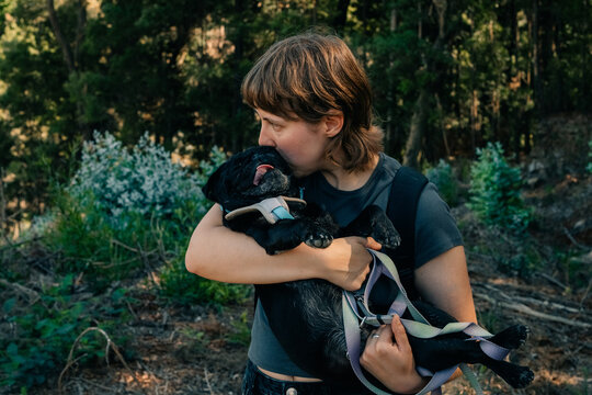 Woman Carrying a Black Puppy in a Forest Setting During Daylight