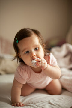 Baby Girl Crawling on Bed with Pacifier at Home