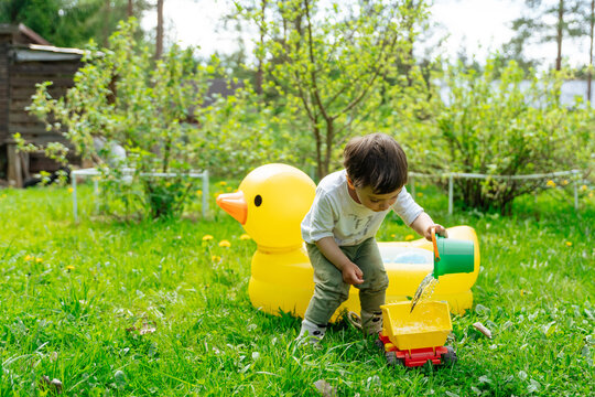 Child pouring water into toy truck beside inflatable duck tub 