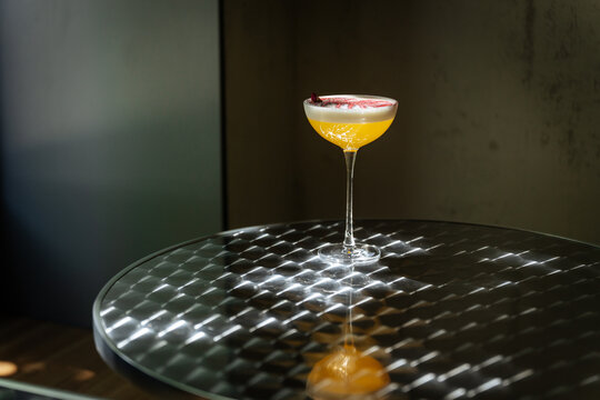 Elegant yellow cocktail with foam and garnish on reflective table