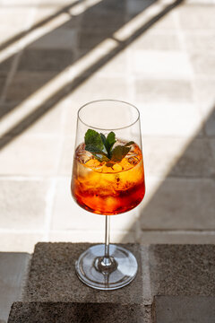 Aperol spritz cocktail with mint garnish on sunny stone surface