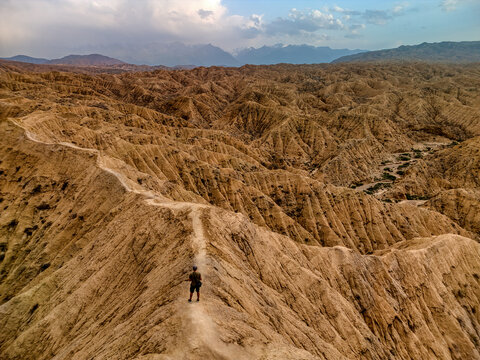 Aerial view of a person standing on a narrow ridge overlooking the eroded sandstone formations of Kan'on Aksay under a cloudy sky in Ak Say, Issyk-Kul Region, Kyrgyzstan.