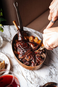 Slicing braised lamb shank with roasted potatoes