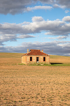Abandoned stone cottage with rusty roof sits in a vast, dry field