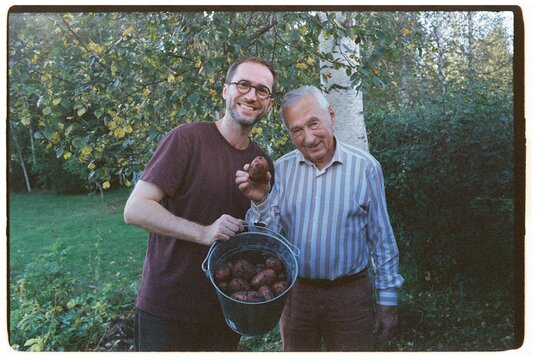An adult grandson and his grandfather are digging potatoes