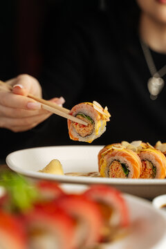 Hand lifting sushi roll with chopsticks over plate