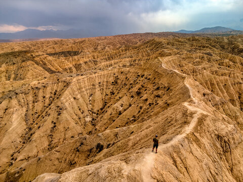 Aerial view of a person standing on a narrow ridge overlooking the eroded sandstone formations of Kan'on Aksay under a cloudy sky in Ak Say, Issyk-Kul Region, Kyrgyzstan.