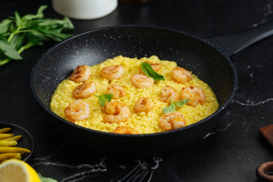 Saffron risotto with grilled shrimp and basil in a frying pan