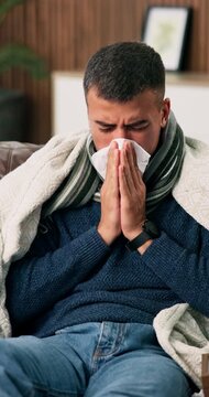 Sick, man and blowing nose in house with tissue, sinus infection and blanket for influenza symptoms. Person, allergies and health problem in living room with toilet paper, illness or germs from virus