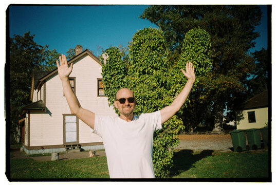 Man Enjoys Sunny Day Outside House With Green Shrub Backdrop