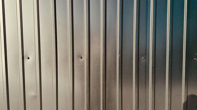 Corrugated metal fence panels shimmering in sunlight, closeup of galvanized steel ridges with subtle dents and visible screws.
